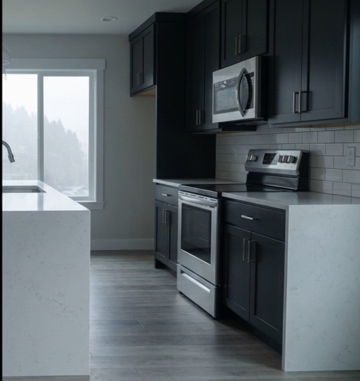 Saanich kitchen after SafeBuild renovation — dark shaker cabinetry, quartz waterfall counters, subway tile, stainless appliances, refinished oak floors